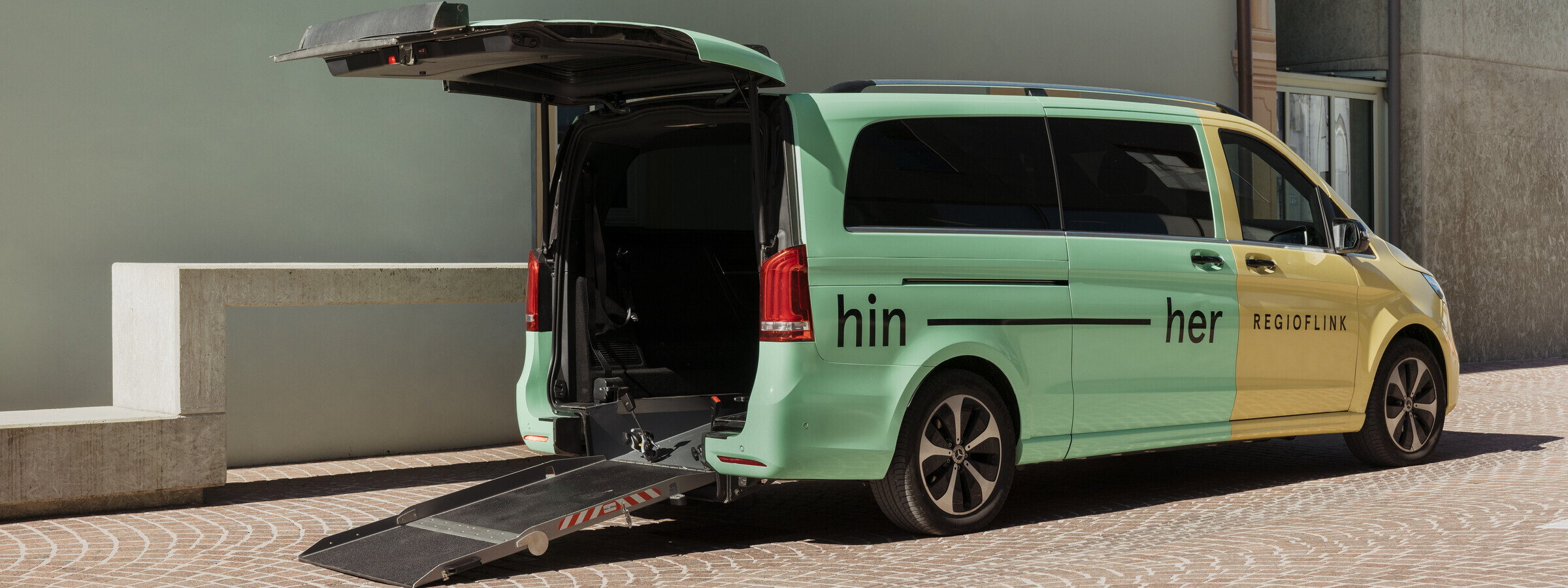 Abgebildet ist ein Regioflink Auto mit geöffnetem Kofferraum und ausgefahrener Rampe für einen barrierefreien Einstieg. Das Auto steht vor einem Gebäude.