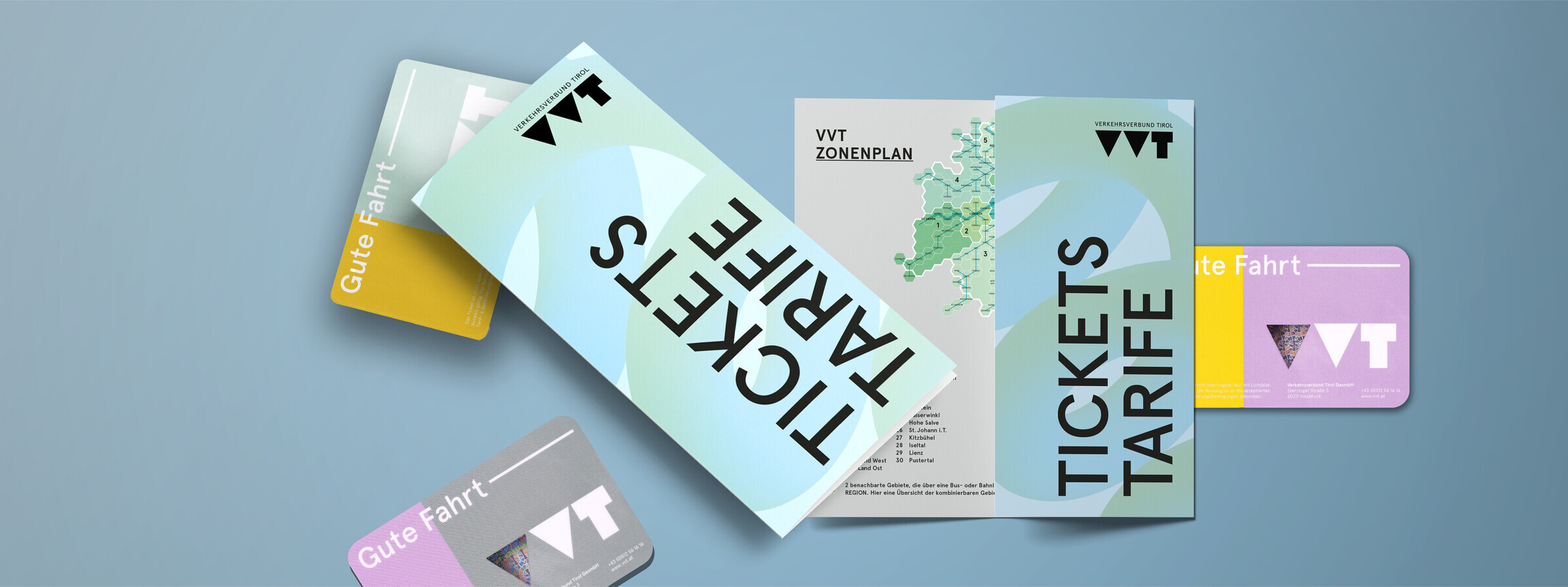 Mehrere VVT-Broschüren und Fahrkarten liegen auf einem blauen Hintergrund verteilt. Die Broschüren zeigen Informationen zu Tarifen und Zonenplänen des Verkehrsverbunds Tirol.