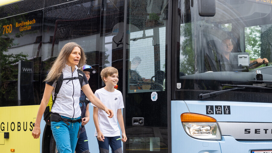 Drei Personen gehen neben einem Bus.