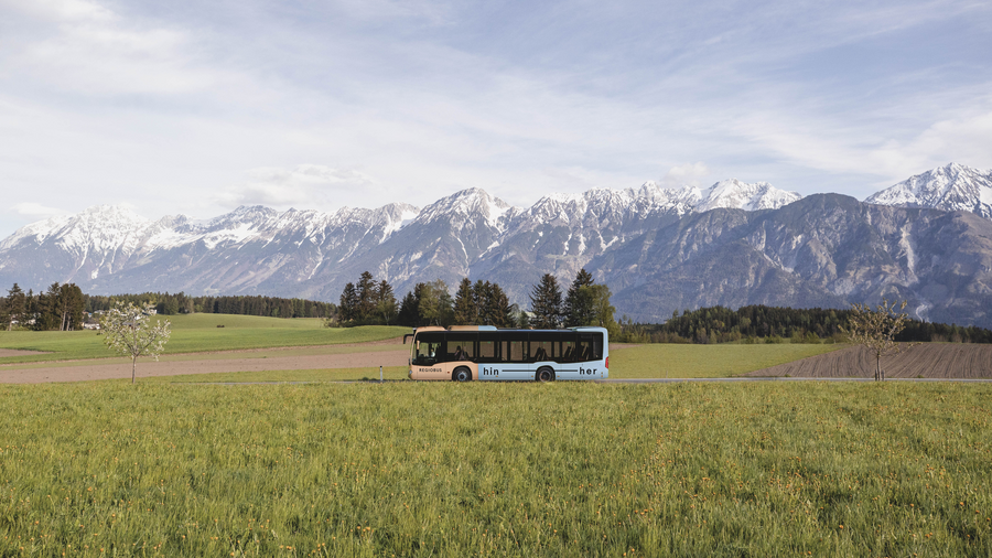 Bus fährt in sommerlicher Landschaft vor Bergkette